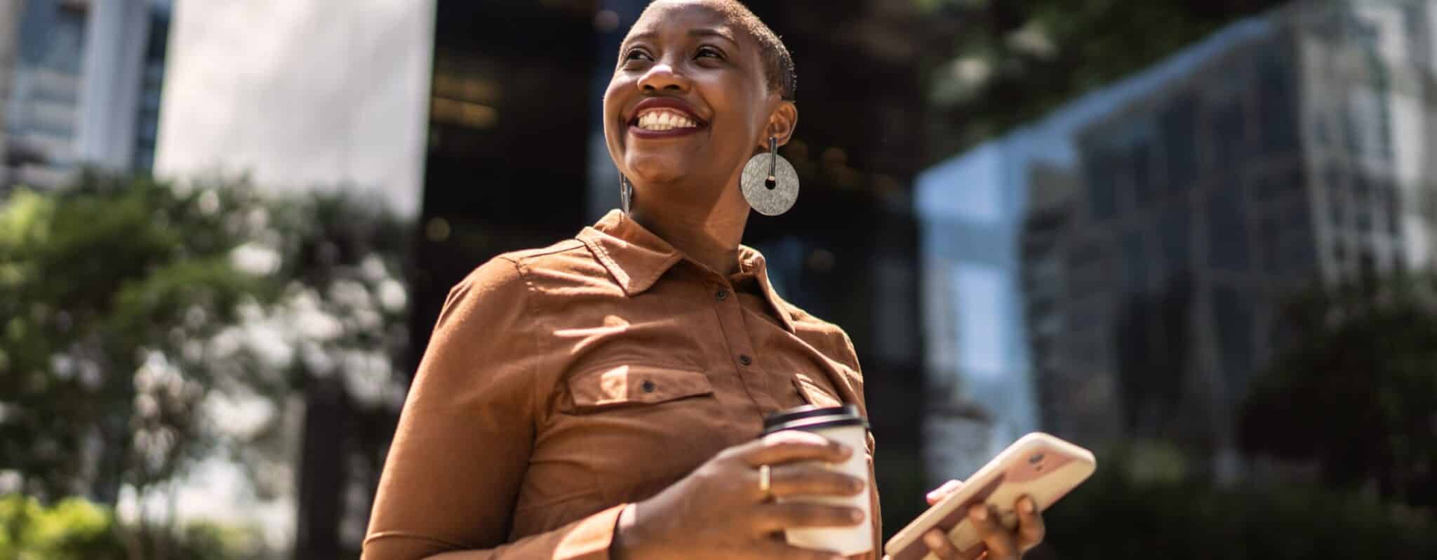 Woman smiling while holding a coffee and a cellphone